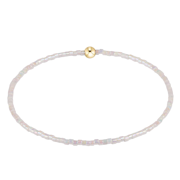 Thin white beaded bracelet with a gold clasp on a white background