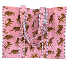 Pink quilt with brown tiger pattern on a metal surface against a brick wall background