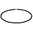 A beaded necklace made of small black faceted beads with a single round gold clasp, displayed on a clean white background.