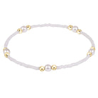 A delicate beaded bracelet with white faux pearls and polished gold spacer beads, arranged in a circle on a clean white background.
