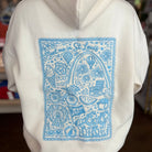 A person wearing a white hoodie with a large light blue graphic print on the back featuring illustrations and the text 'Meet me in St. Louis'.