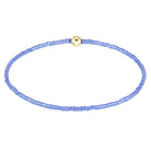 A delicate beaded bracelet made of small iridescent light blue beads with a central gold-toned round charm, displayed on a clean white background.