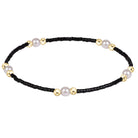 A delicate beaded bracelet featuring a black bead chain accented with large white pearls and polished gold spacer beads, displayed on a clean white background.