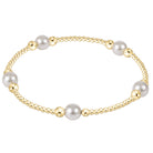 A gold beaded bracelet with six large white pearls spaced evenly, displayed on a clean white background.